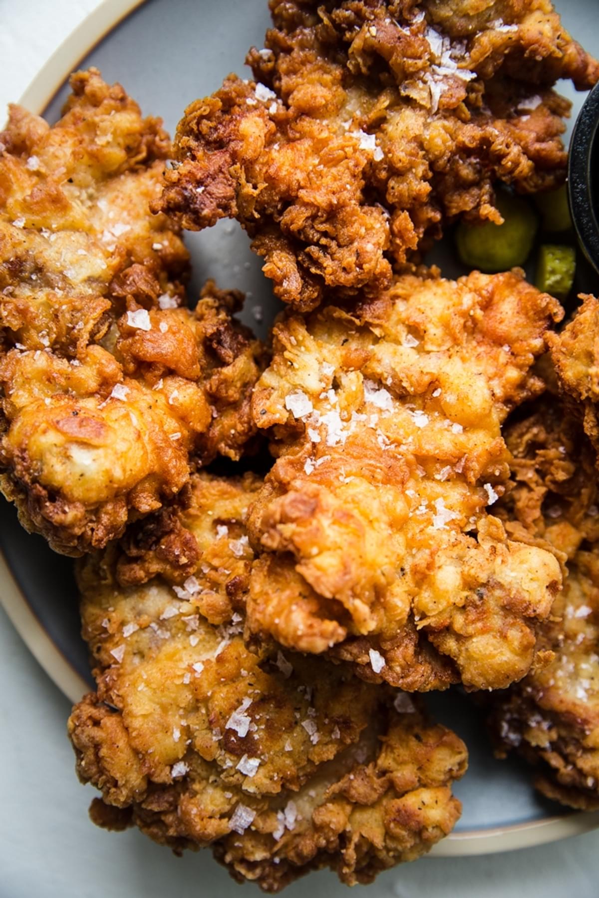 Fried chicken on a light blue platter shown close up topped with flaky salt.