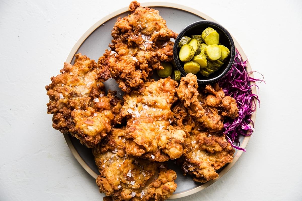 Light blue platter of fried boneless skinless chicken thighs shown with sliced pickled and pickled cabbage.
