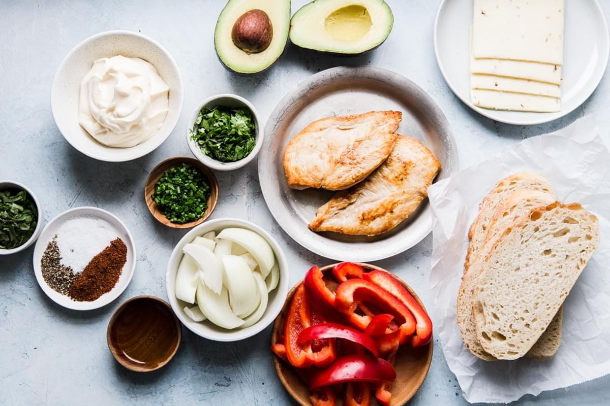 Ingredients shown for a grilled chicken sandwich including onions, peppers, pepper jack cheese, sourdough bread and avocado.