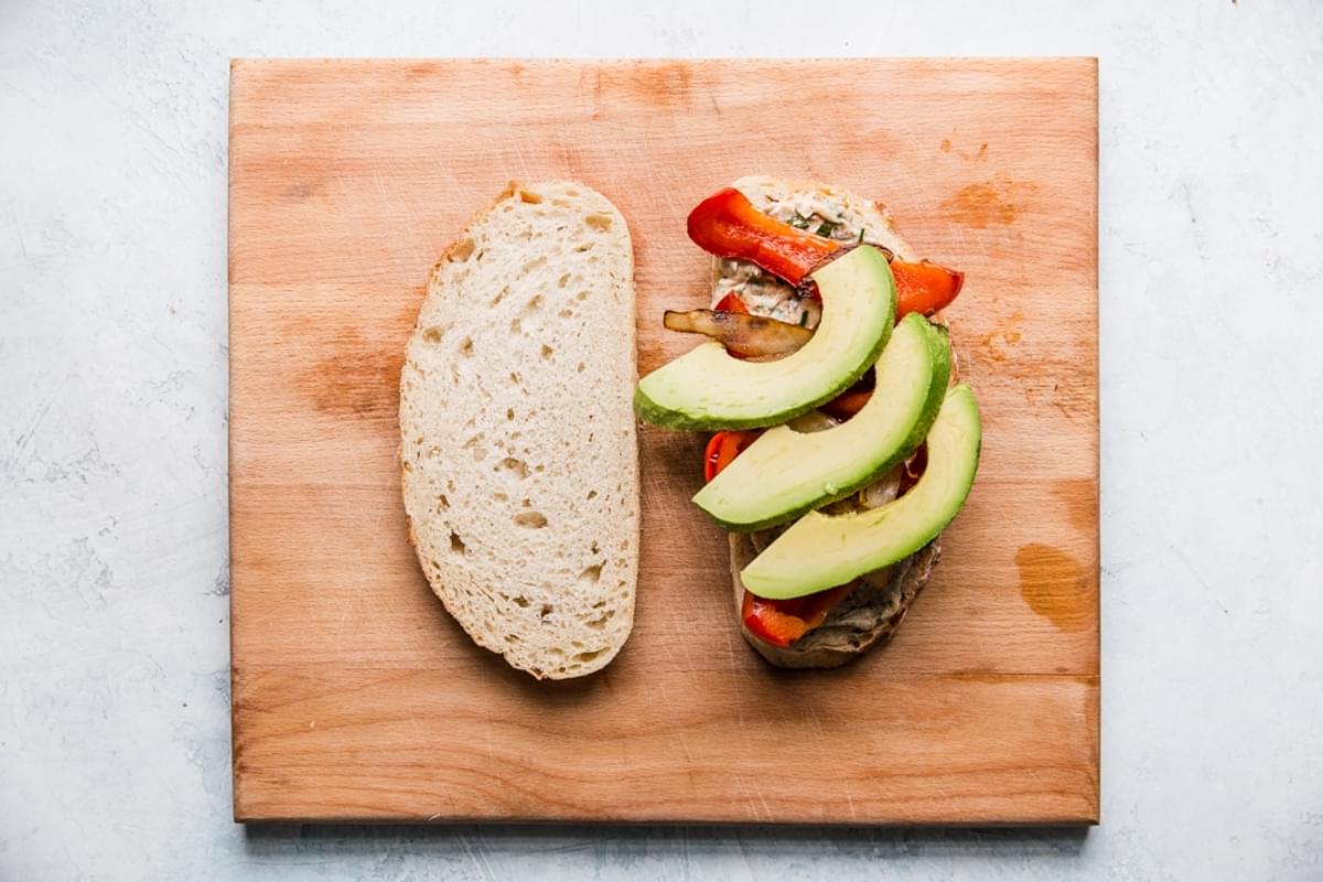 two slices of sourdough bread with herbed mayo, onions, bell peppers and avocados on one side.