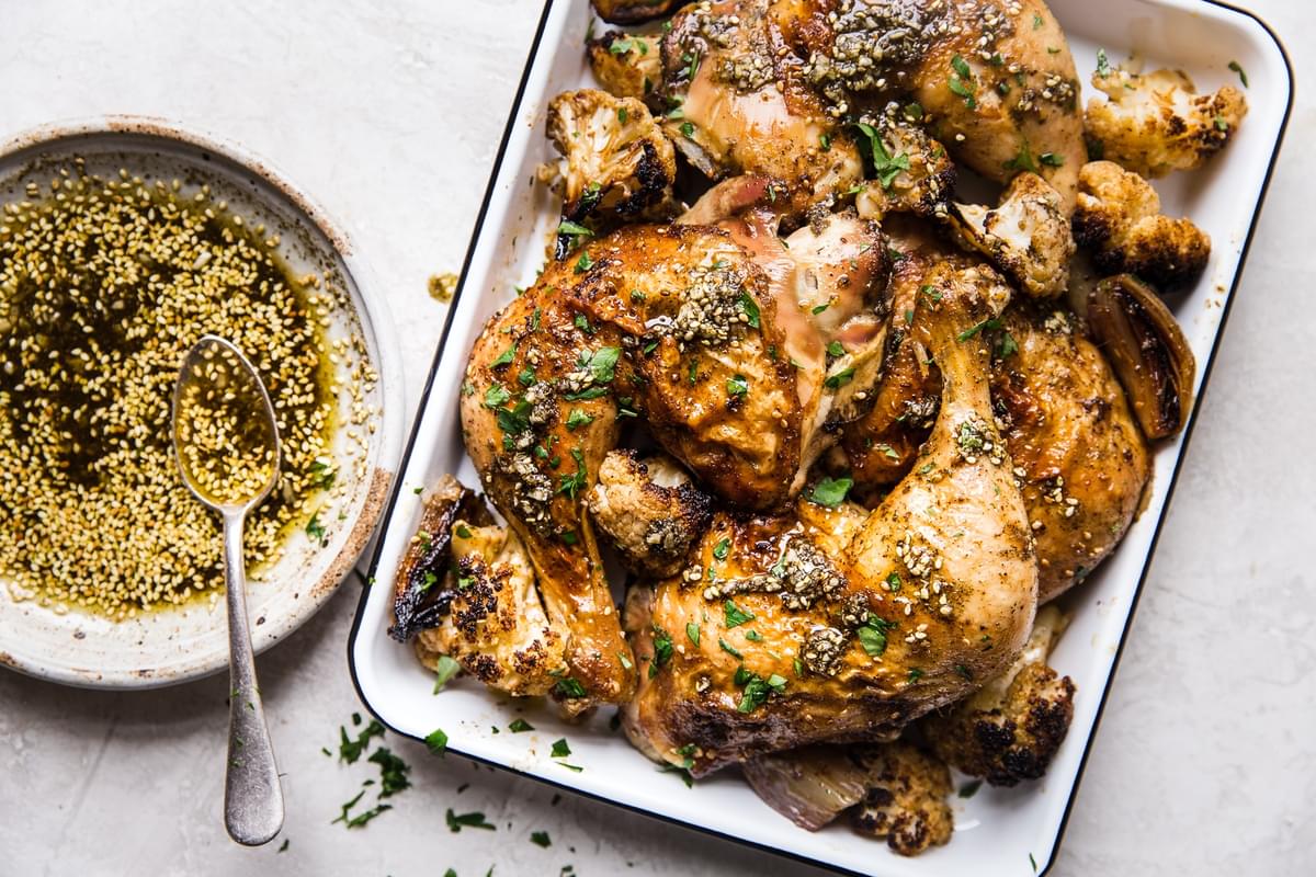 za'atar chicken in a roasting pan with cauliflower and shallots next to a bowl of za'atar oil