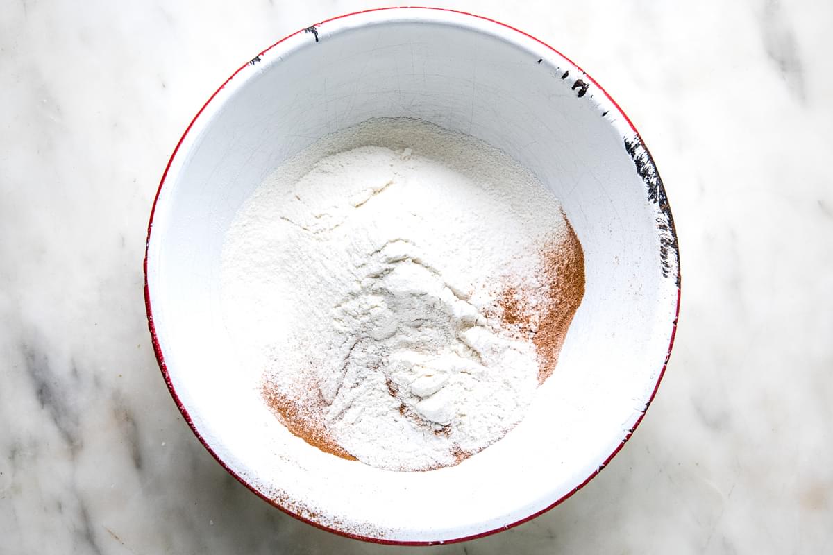 flour, baking powder, baking soda, salt and cinnamon sifted together in a bowl on the counter