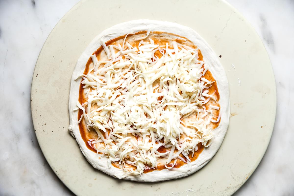 Pizza sauce spread on pizza dough with bbq sauce and grated cheese.