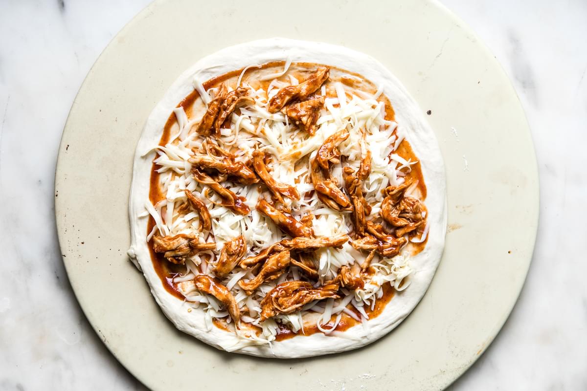 pizza dough topped with grated cheese, bbq sauce and shredded chicken.