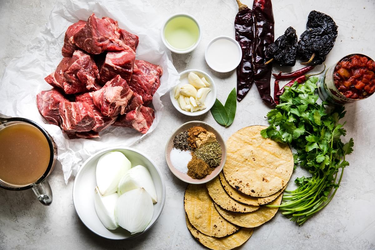 Beef Birria Ingredients laid out on a counter Chuck roast, chiles, cilantro, onion, spices and corn tortillas