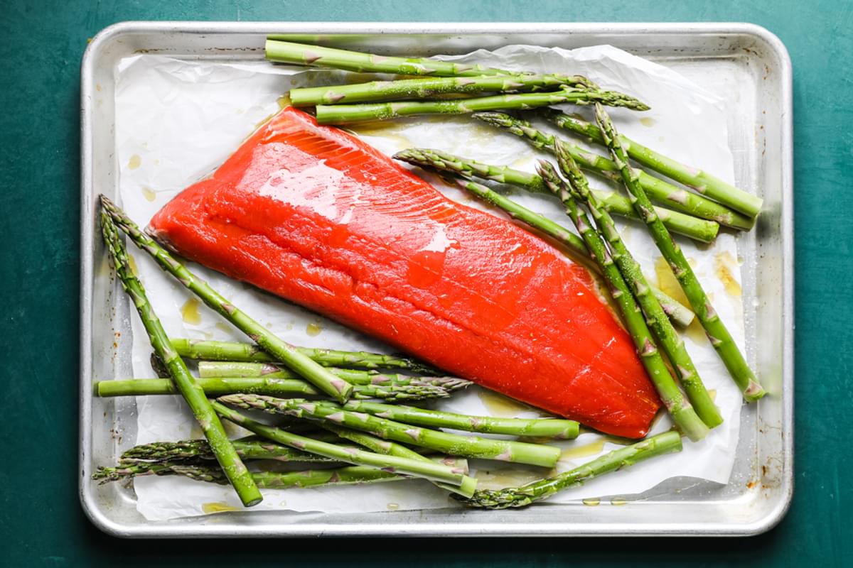 fillet of salmon and asparagus on a baking sheet with parchment and olive oil