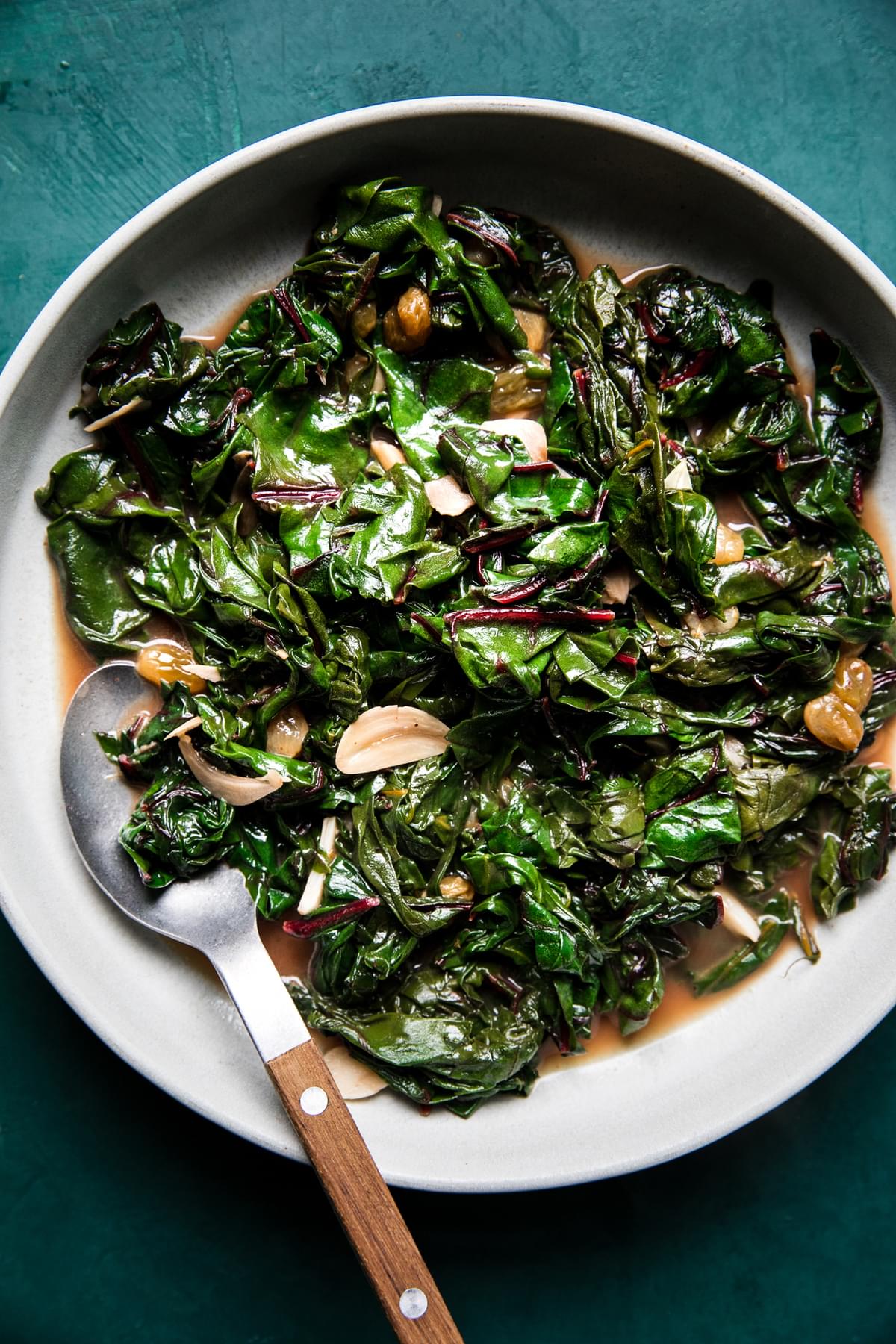 Braised Greens with Golden Raisins and Maple in a serving bowl with spoon