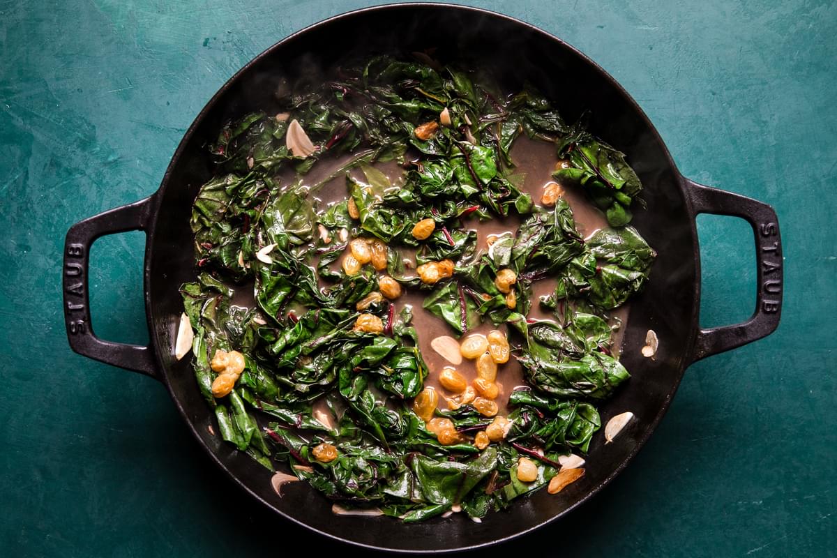 ingredients for braised greens with golden raisins and maple cooking in a skillet