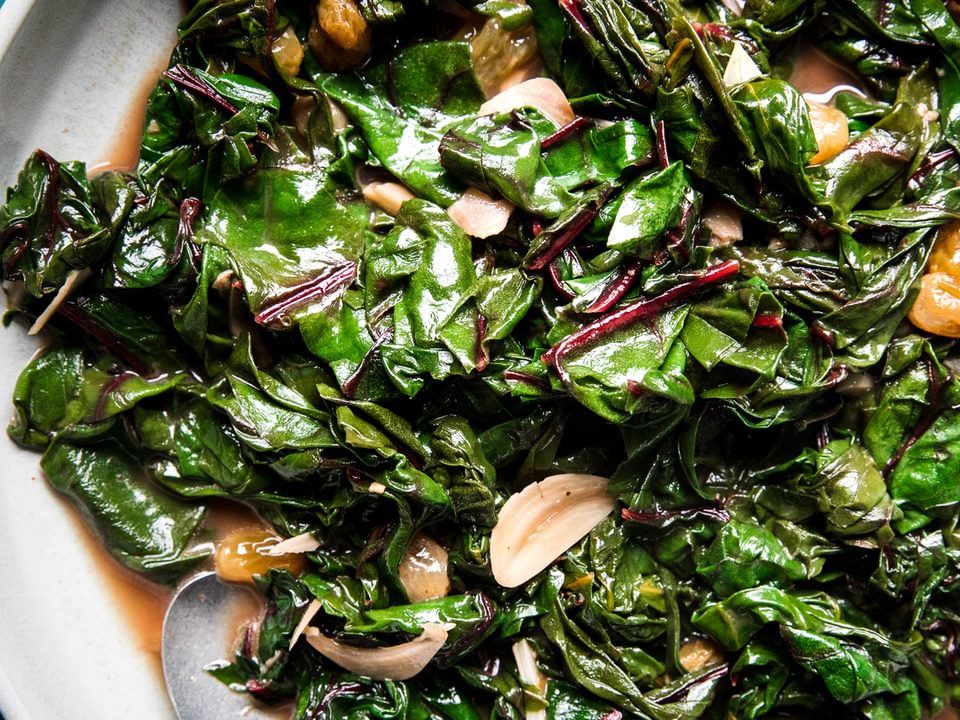 Braised Greens with Golden Raisins and Maple in a serving dish with a serving spoon