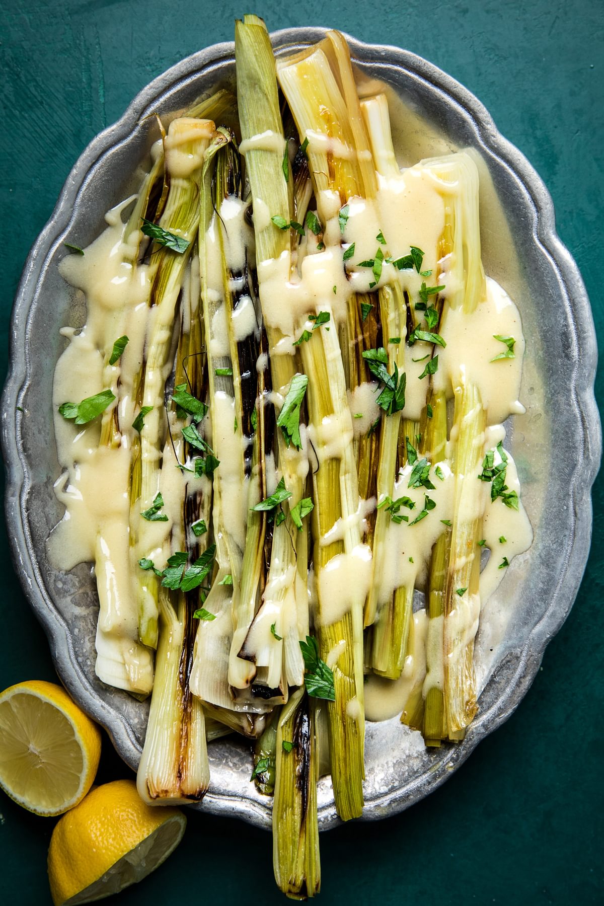 Braised Leeks with Beurre Blanc (French Butter Sauce) on a serving platter with a halved lemon beside it