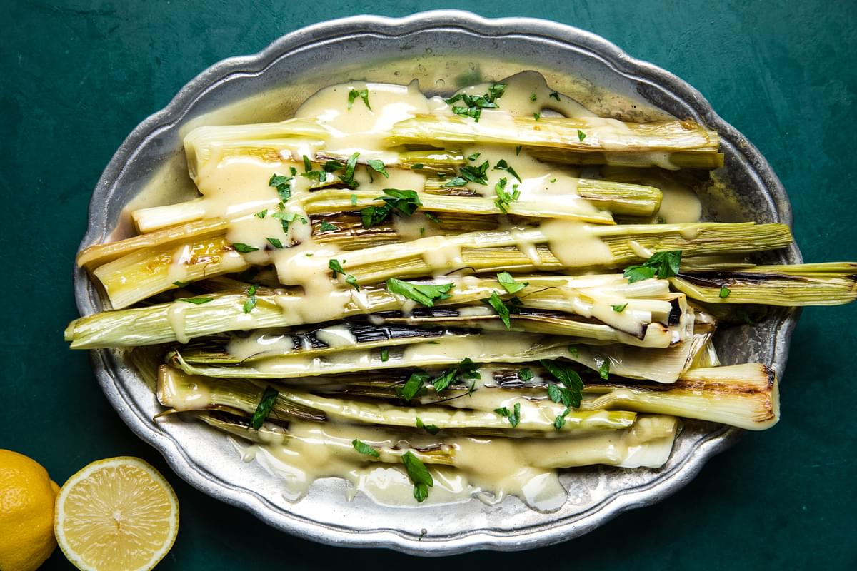 Braised Leeks with Beurre Blanc (French Butter Sauce) on a serving platter with a halved lemon beside it