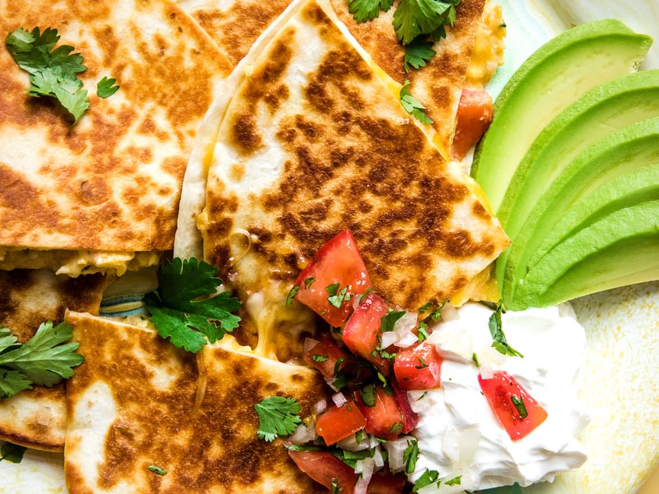 a breakfast quesadilla filled with cheese, bacon, eggs and pico de Gallo on a plate with avocado and sour cream