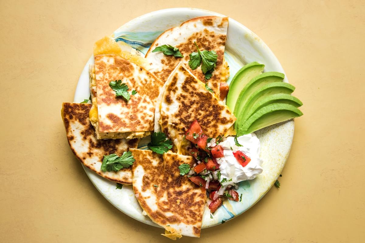 a breakfast quesadilla  filled with scrambled eggs, pico de Gallo, bacon and cheese on a plate with avocado and sour cream