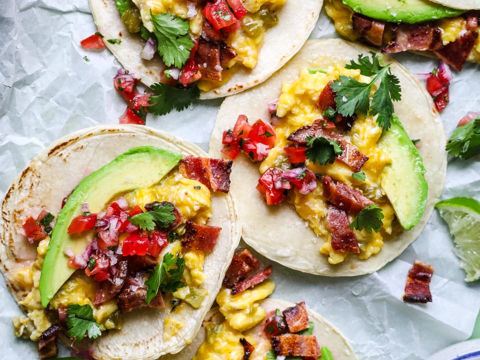 breakfast tacos with green cilia, bacon, avocado and cheddar cheese on parchment paper
