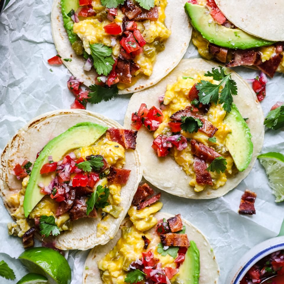 breakfast tacos with green cilia, bacon, avocado and cheddar cheese on parchment paper