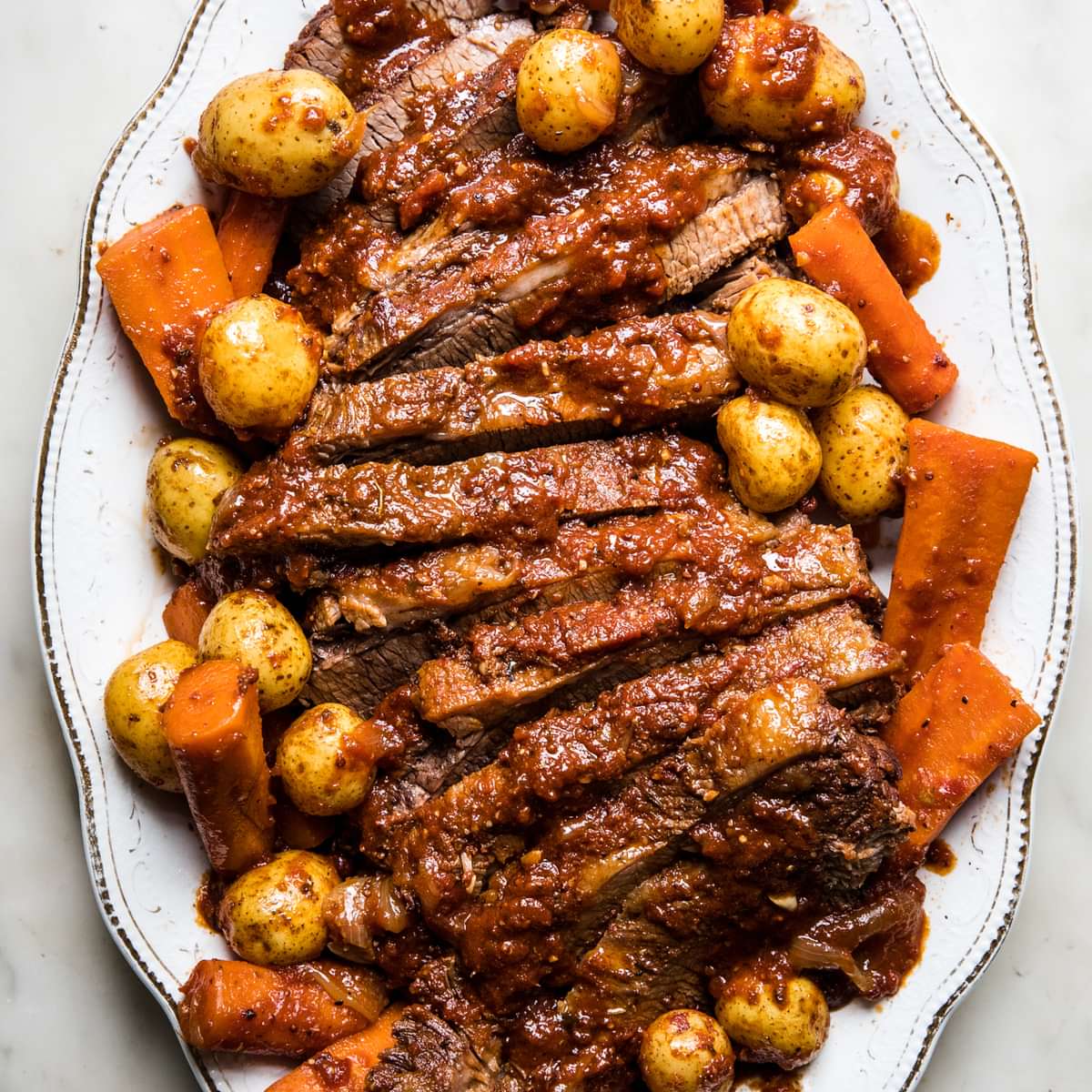 homemade braised brisket sliced on a serving platter nestled with carrots and potatoes