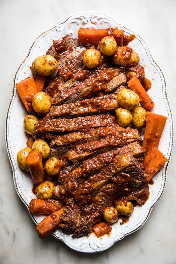 homemade braised brisket sliced on a serving platter nestled with carrots and potatoes