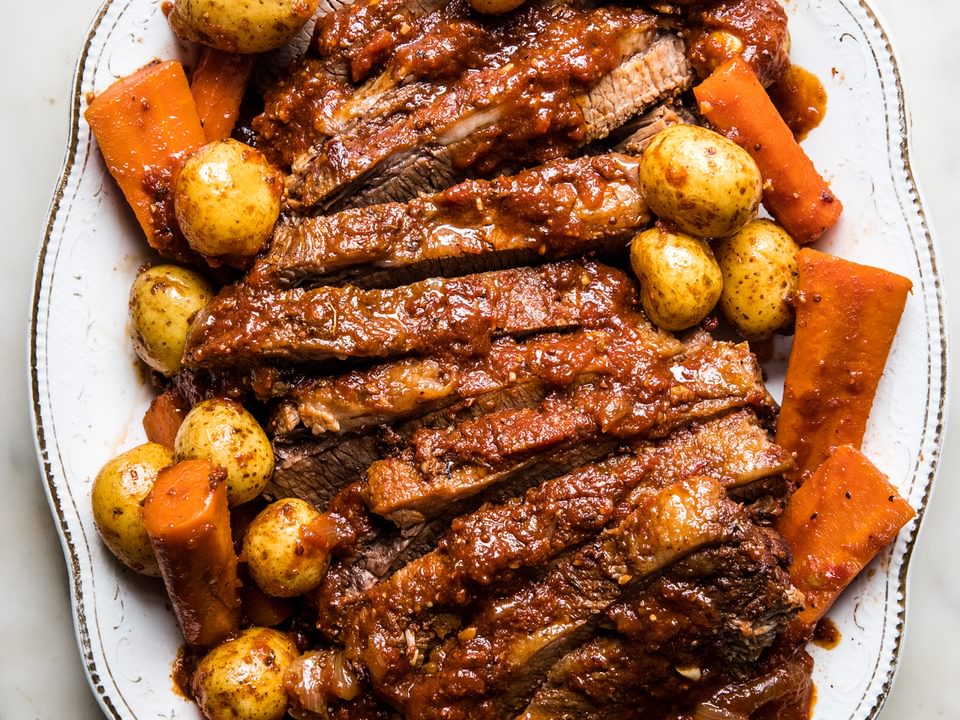 homemade Jewish brisket sliced on a serving platter nestled with carrots and potatoes