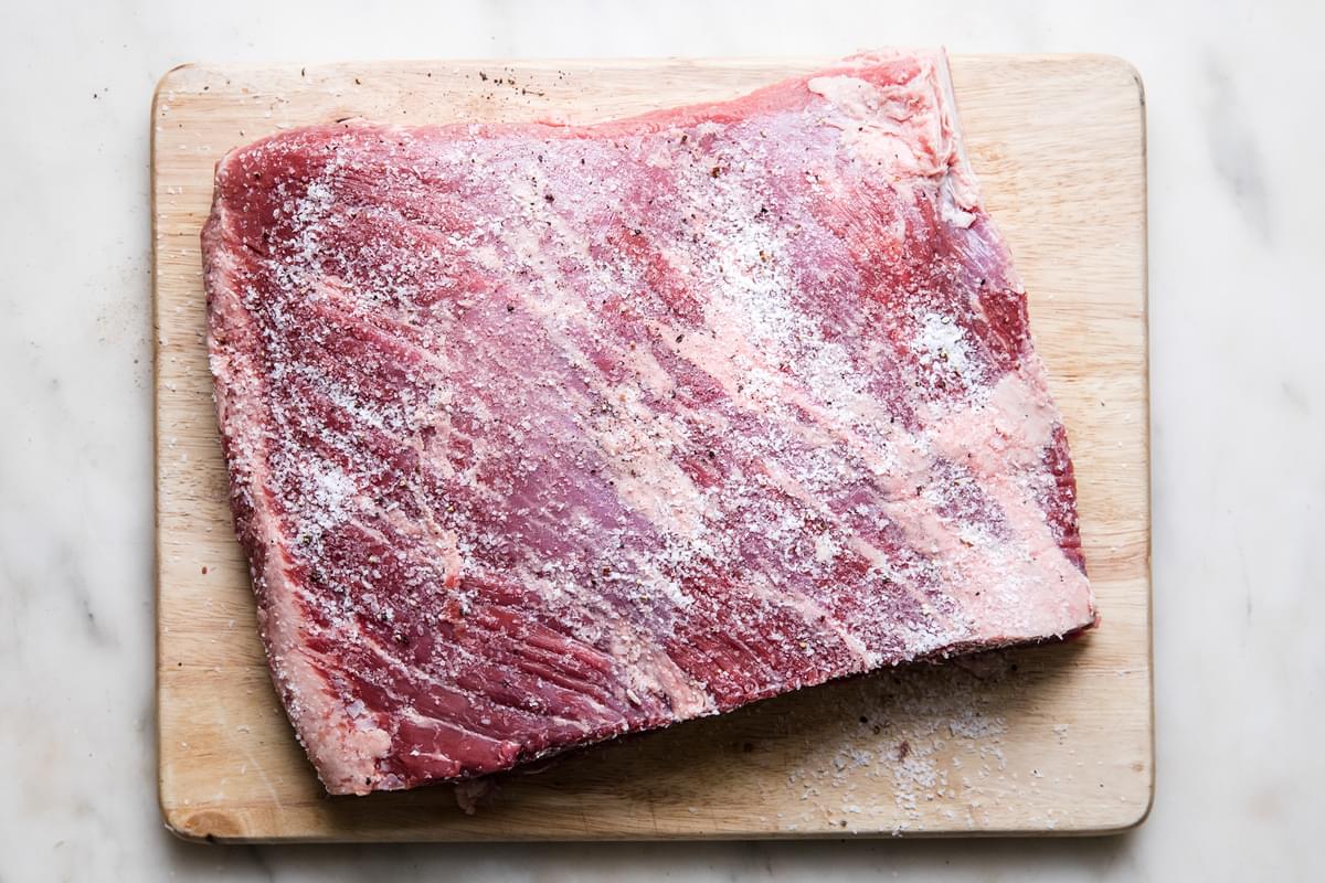 raw beef brisket seasoned with salt and pepper on a cutting board