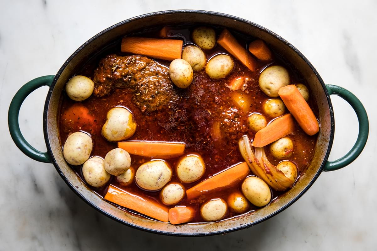 Braised brisket, carrots, potatoes and onions nestled in sauce in a dutch oven