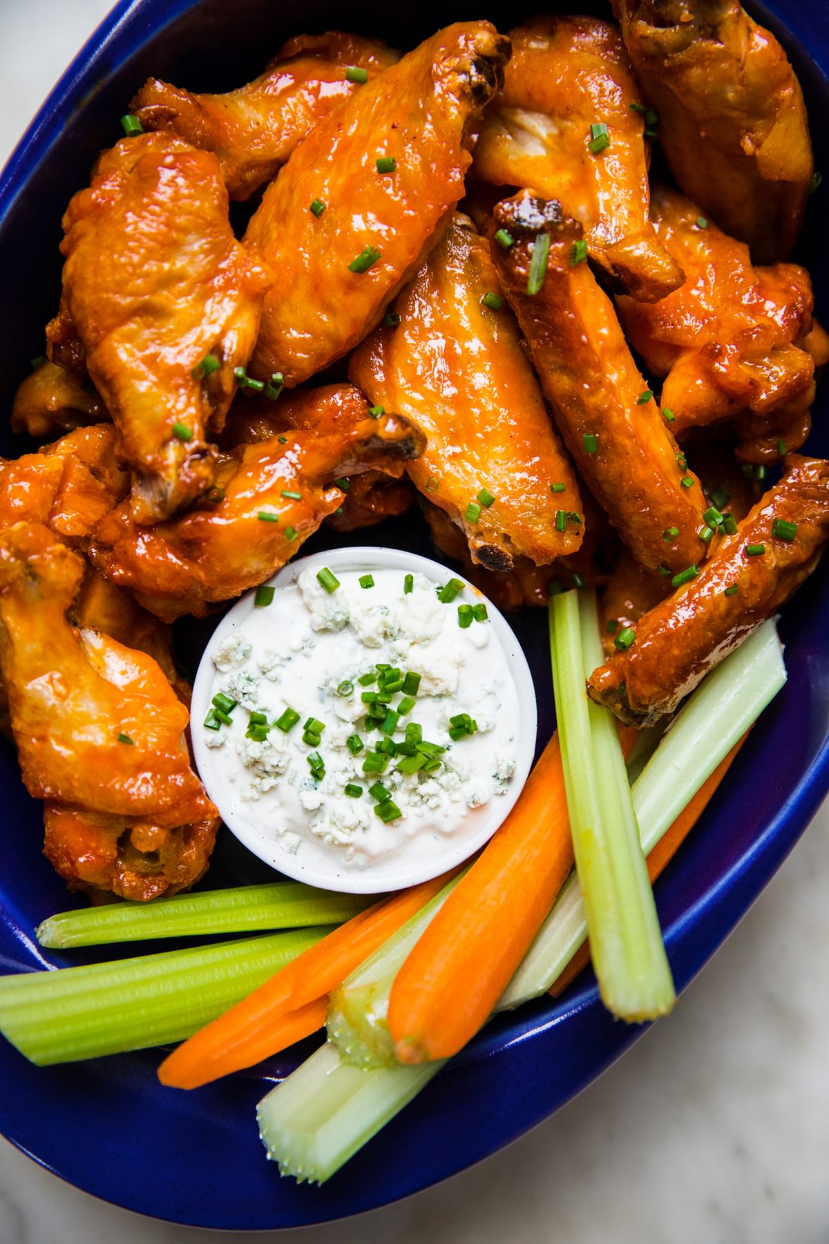 homemade baked buffalo wings on a serving platter with blue cheese dressing and carrot and celery sticks