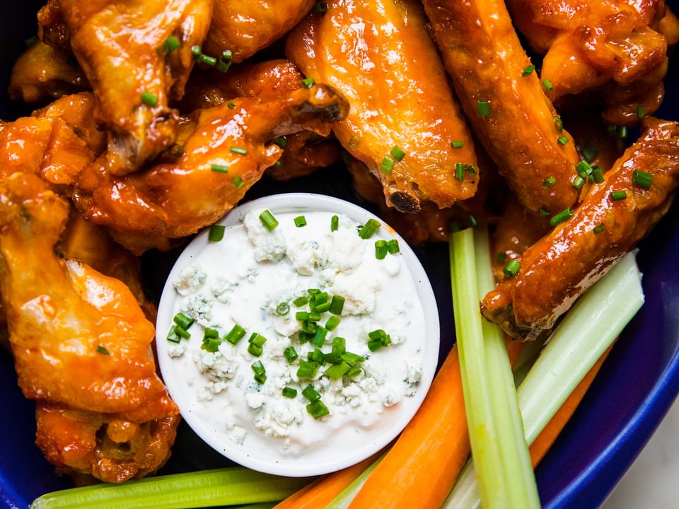 homemade baked buffalo wings on a serving platter with blue cheese dressing and carrot and celery sticks