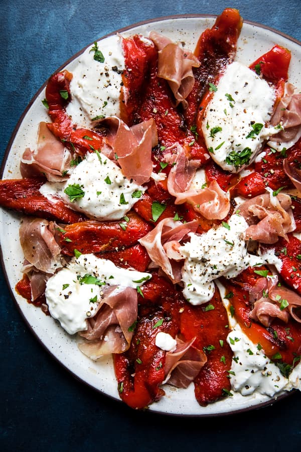 a plate of homemade roasted red peppers with Prosciutto and burrata