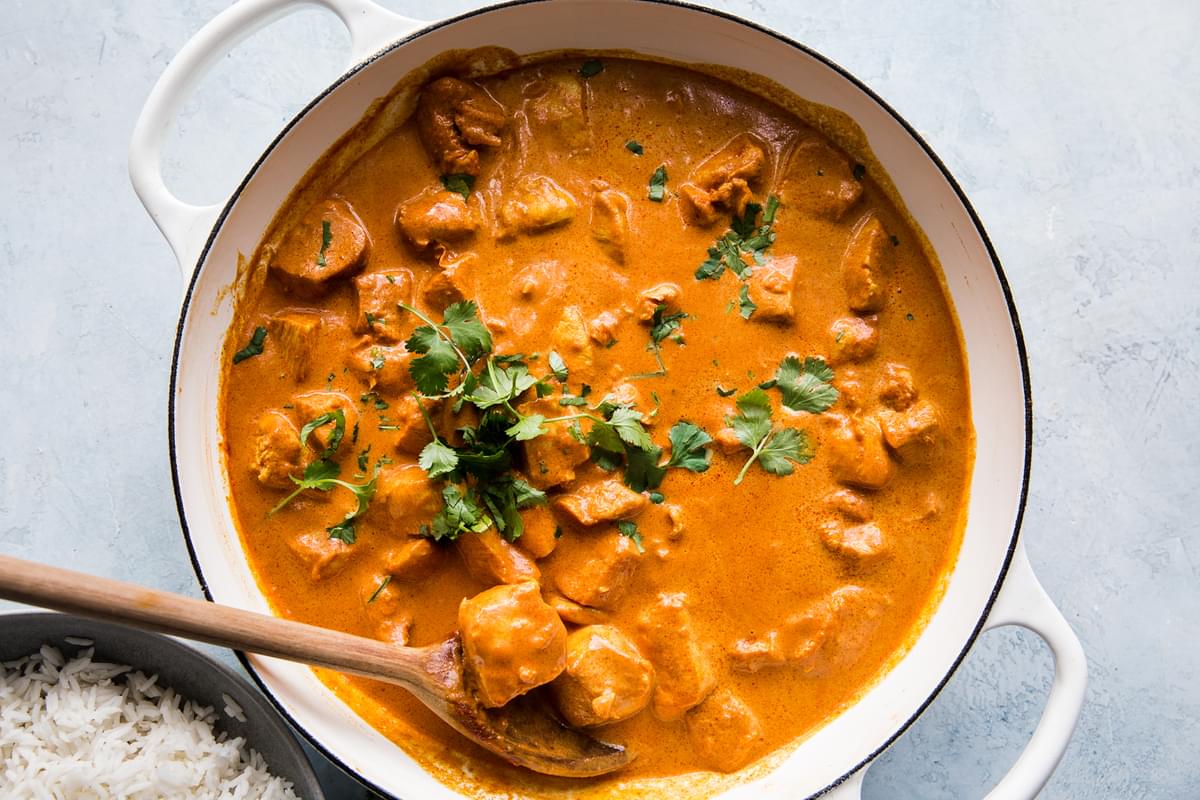butter chicken in white pot with a wooden spoon and cilantro