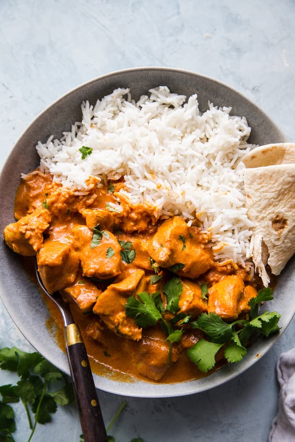 homemade butter chicken recipe in a bowl served with rice and naan