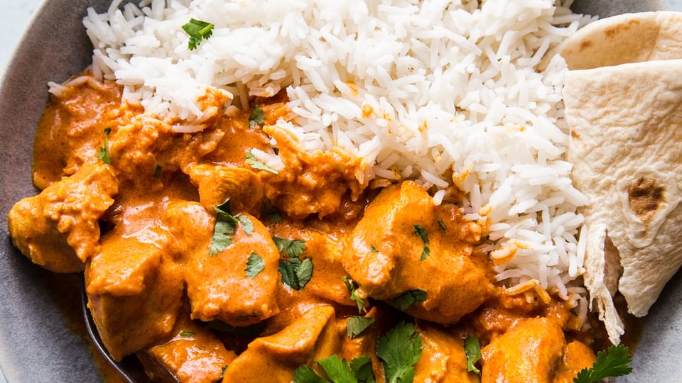 homemade butter chicken recipe in a bowl served with rice and naan