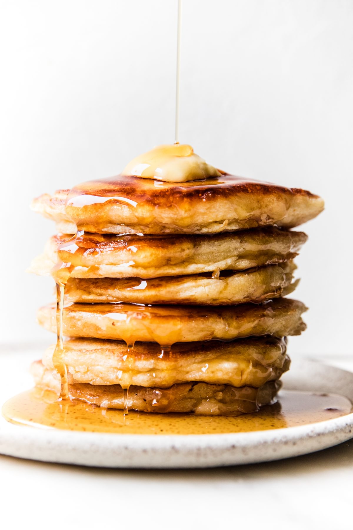 stack of buttermilk pancakes topped with butter and dripping with syrup