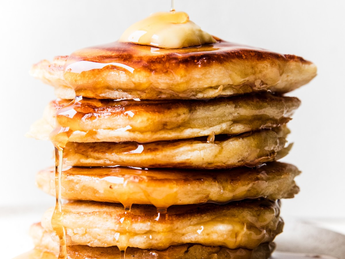 stack of buttermilk pancakes topped with butter and dripping with syrup