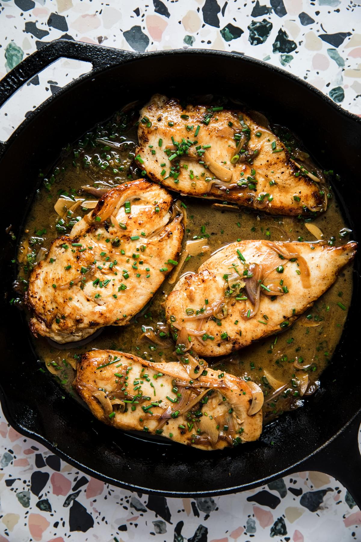 chicken paillard in a cast iron pan with chives, shallots and garlic