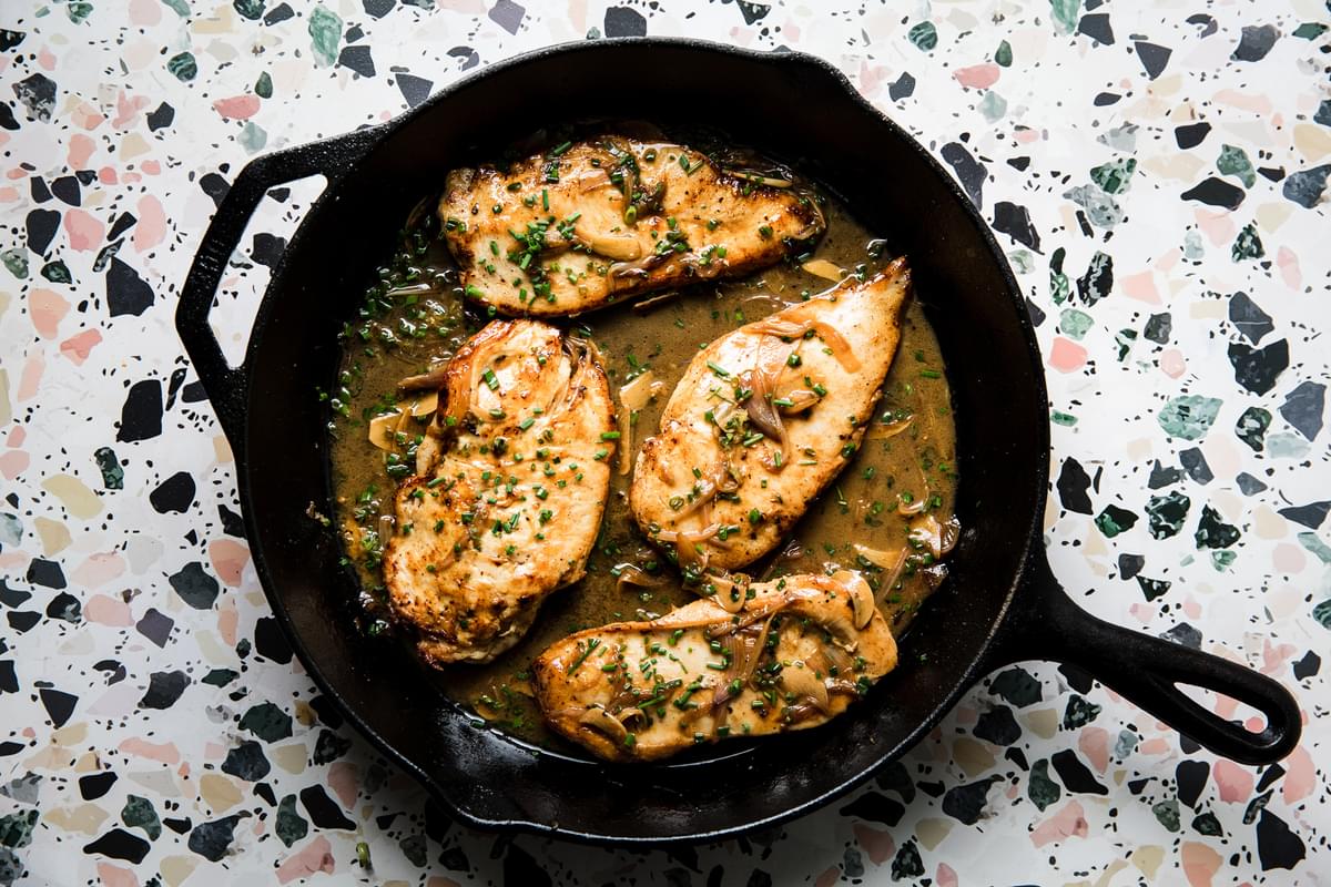 chicken paillard with butter and olive oil, garlic, shallots and chives in a cast iron skillet
