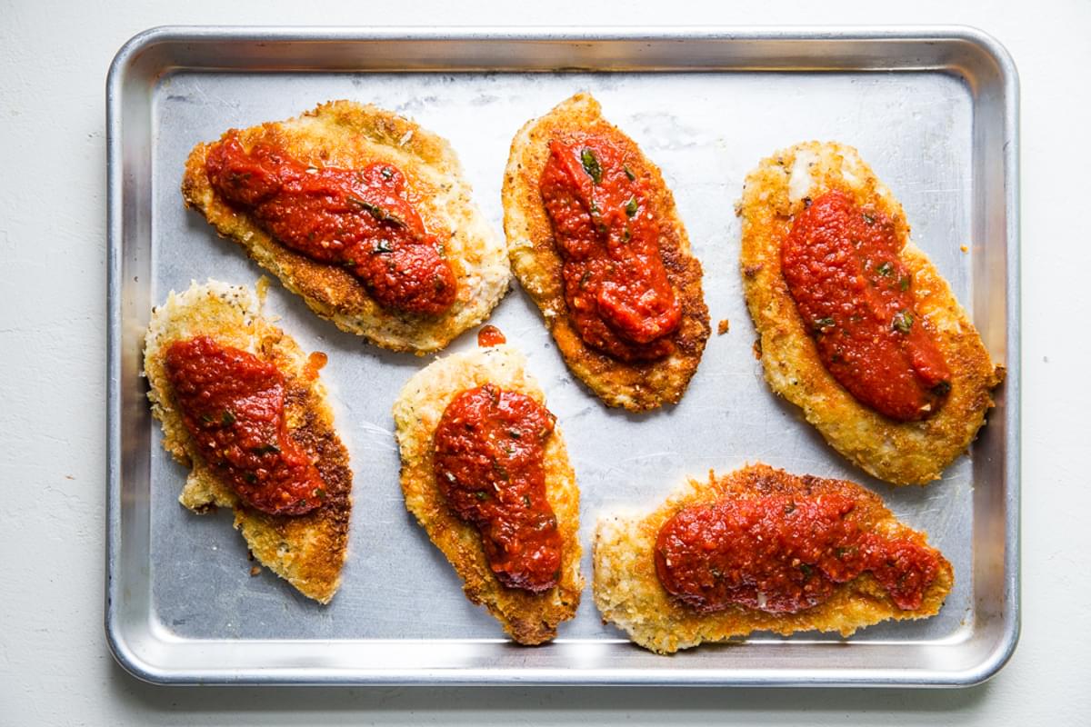 pan fried breaded chicken breast on a baking sheet with marinara