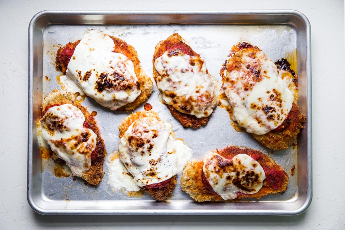 pan fried breaded chicken breast on a baking sheet baked with marinara and mozzarella