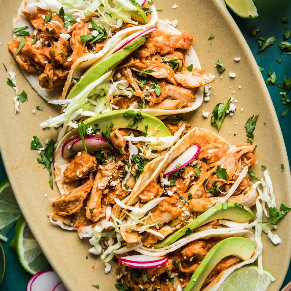 chicken tinga tacos in a platter with avocado and radishes