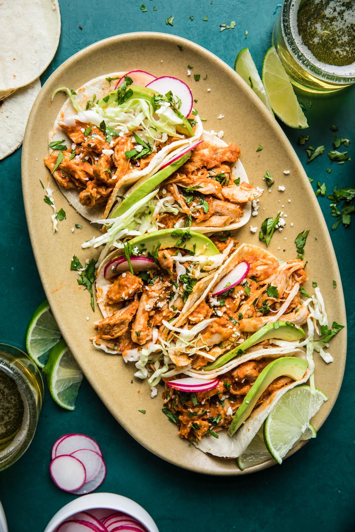 chicken tinga tacos on a platter with avocado and radishes