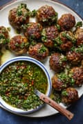 Chimichurri Meatballs on a plate with a bowl of chimichurri sauce