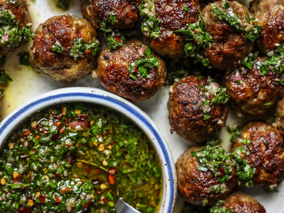Chimichurri Meatballs on a plate with a bowl of chimichurri sauce