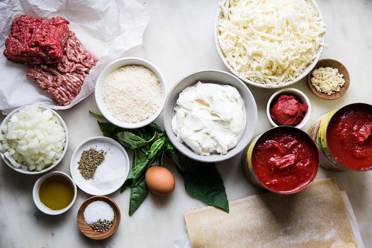 Ingredients for homemade lasagna. canned tomatoes, garlic, noodles, mozzarella, parmesan, ricotta, onions, ground meat