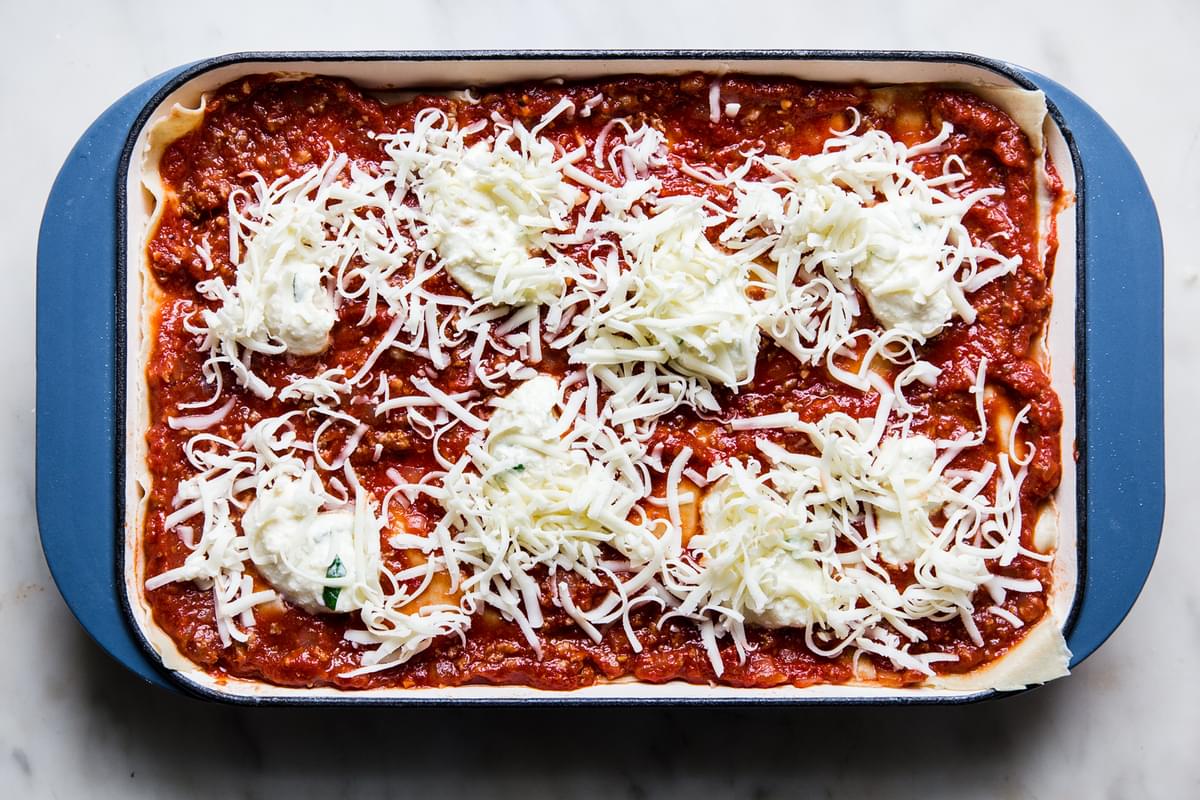 marinara meat sauce in the bottom of a lasagna pan topped with lasagna noodles topped with more sauce ricotta and mozzarella