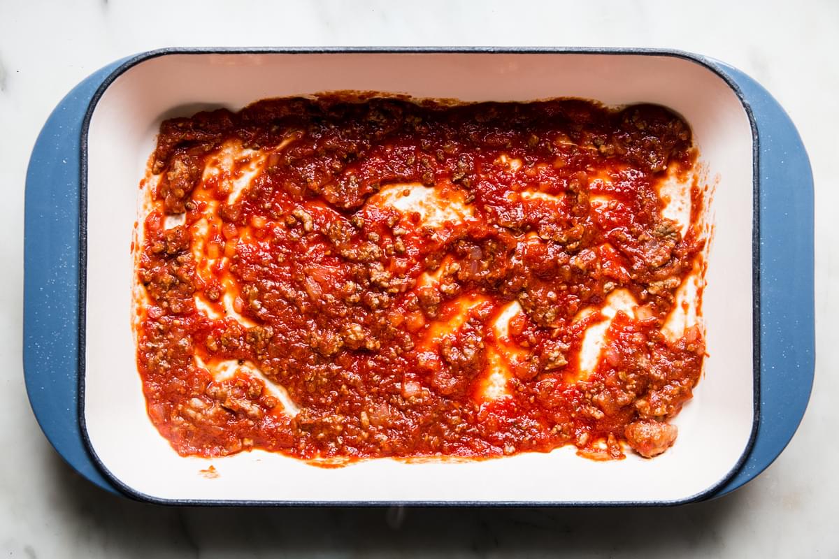 meat sauce with marinara in the bottom of a lasagna pan