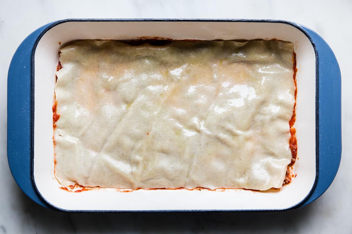 marinara meat sauce in the bottom of a lasagna pan topped with lasagna noodles