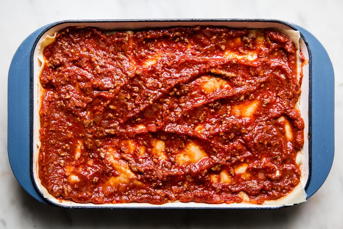 marinara meat sauce in the bottom of a lasagna pan topped with lasagna noodles topped with more sauce