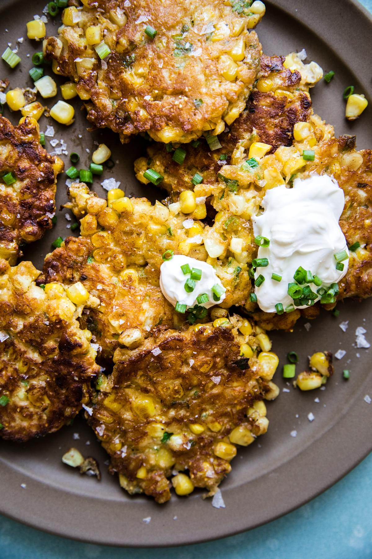 homemade corn fritters a plate with sour cream and green onions