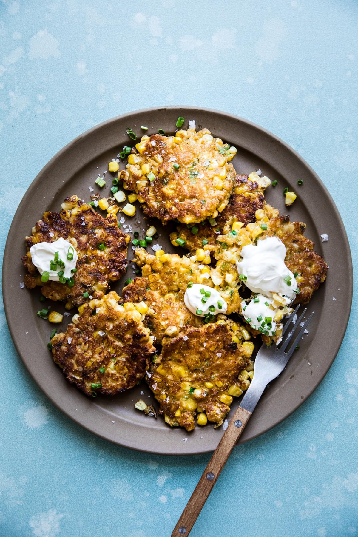 homemade corn fritters a plate with sour cream and green onions