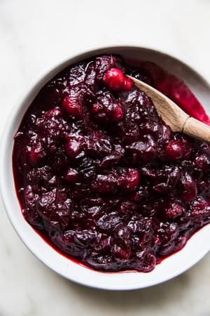 homemade cranberry sauce in a serving bowl with a wooden spoon made with orange juice, cinnamon, cloves and vanilla