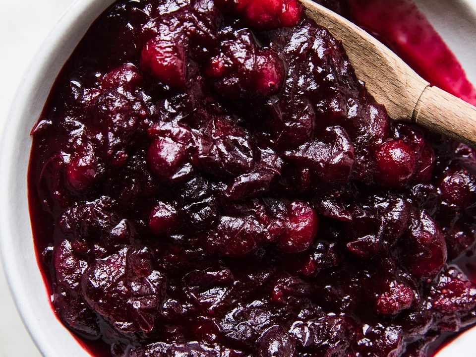 homemade cranberry sauce in a serving bowl on the counter with a wooden spoon