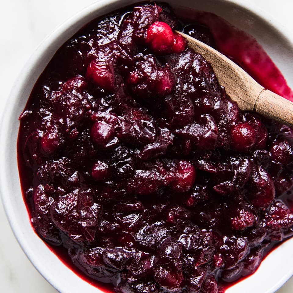 homemade cranberry sauce in a serving bowl on the counter with a wooden spoon